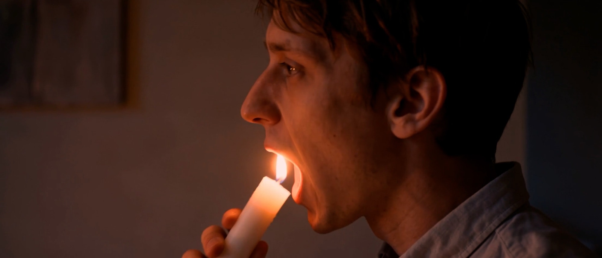 Day one: the scientist holding a lit candle to his mouth in warm light.